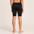 Rear view of a model wearing black shorts against a light beige studio background.