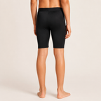 Rear view of a model wearing black shorts against a light beige studio background.